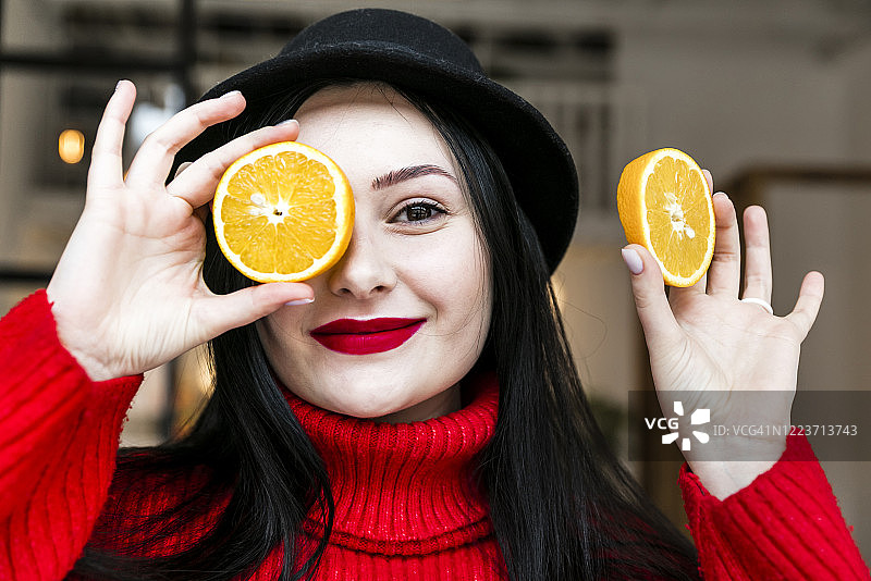 年轻时尚的模特拿着橙子片，在橙色背景下微笑图片素材