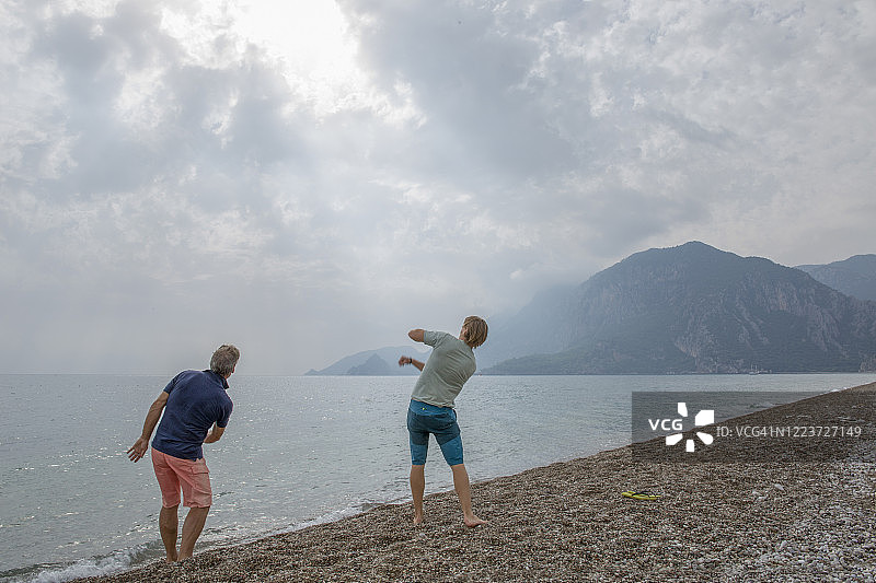 成年儿子和父亲在平静的海面上打水漂图片素材