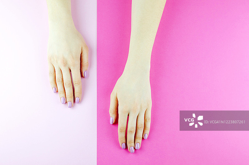 女人的手，在粉红色背景上涂着紫色指甲油图片素材