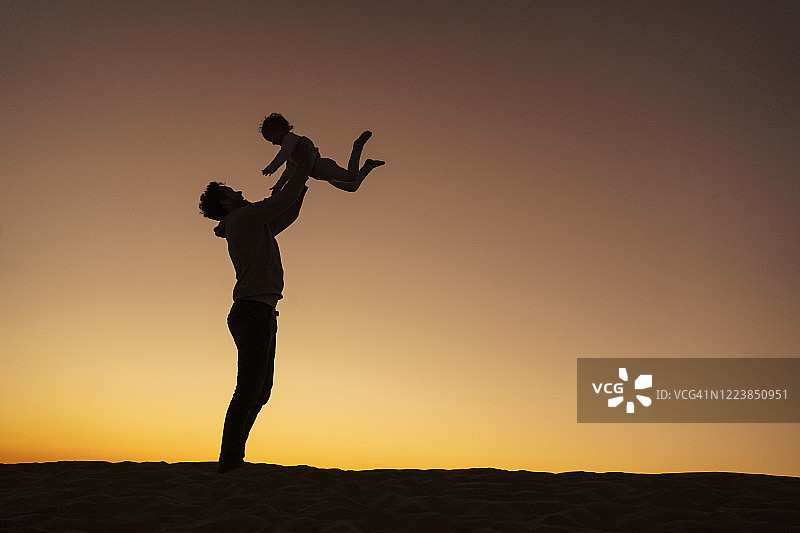 父亲在西班牙大加那利岛日落时分的沙丘上和女儿玩耍图片素材