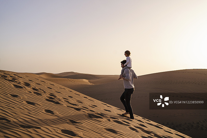 在西班牙大加那利岛的沙丘上，父亲肩上扛着女儿图片素材