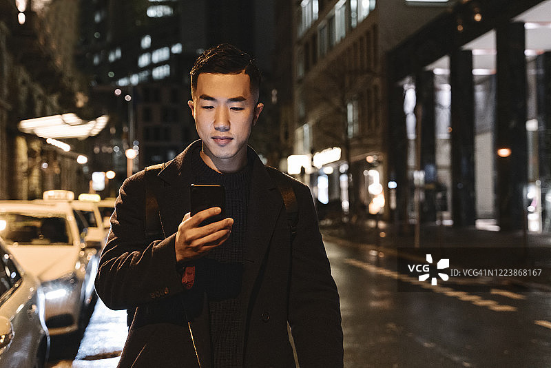 男子夜晚在城市里边走路边使用智能手机图片素材