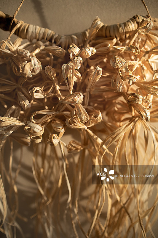 米色墙上手工天然拉菲草编织装饰品，波西米亚风家居装饰和婚礼装饰潮流墙板图片素材