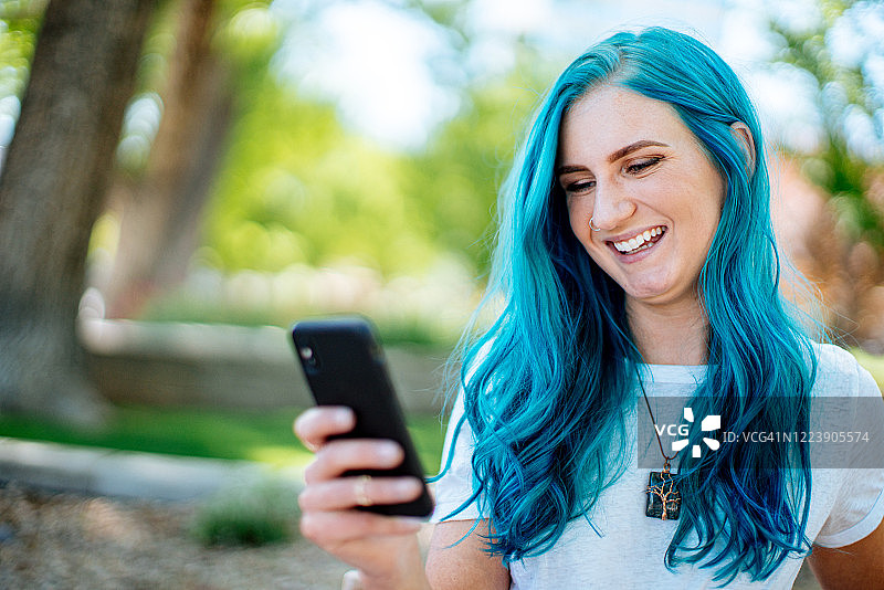 染着蓝绿色头发的时尚年轻女人在夏天户外用手机与朋友聊天图片素材