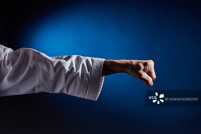 在空手道服中，运动员在蓝色背景上出拳图片素材