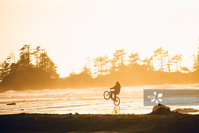男人在日落时分的海滩上骑自行车图片素材