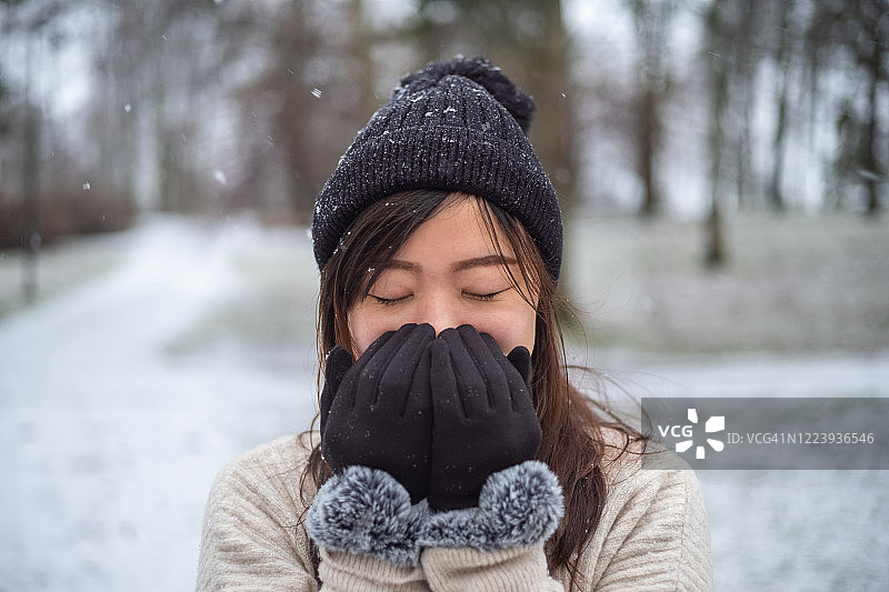 年轻的亚洲女人在冬季公园里热身，用嘴捂住双手图片素材