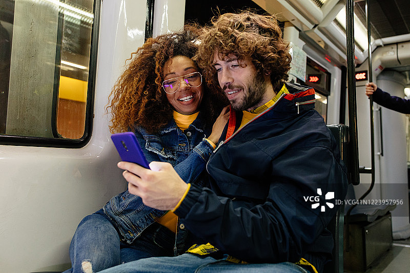 快乐的年轻多民族夫妇坐在火车里使用智能手机图片素材