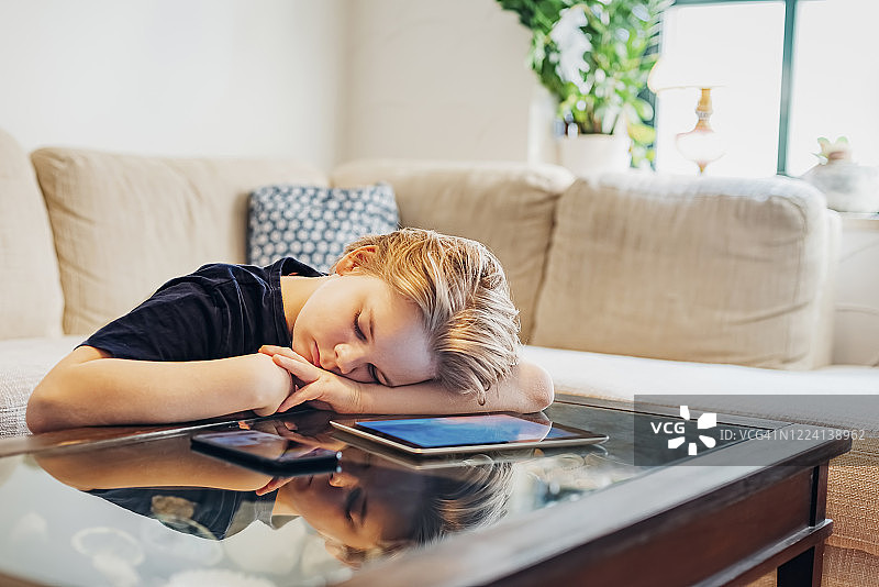 男孩躺在咖啡桌上，拿着智能手机和平板电脑小睡图片素材