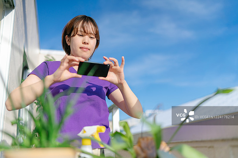 年轻女人在阳台上用智能手机拍摄室内植物图片素材