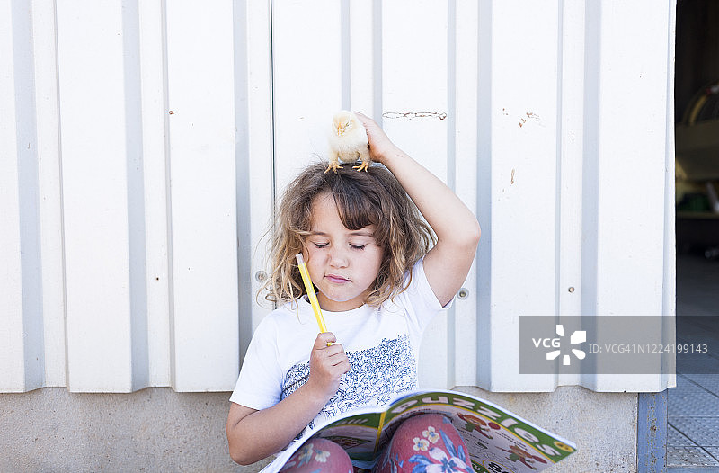 头顶小鸡的可爱小女孩在书中做拼图图片素材