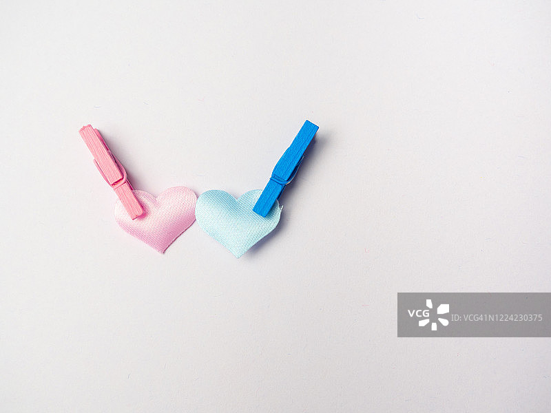 用衣夹连接的粉色和蓝色心形异性恋爱情概念图片素材