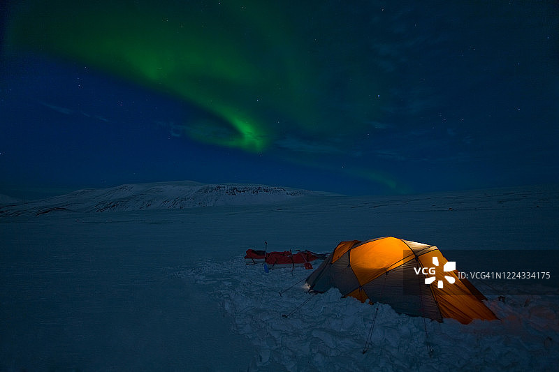 朗格冰川上被照亮的帐篷之上的北极光图片素材