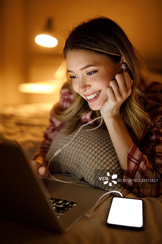 在卧室里晚上看电影的年轻女子图片素材