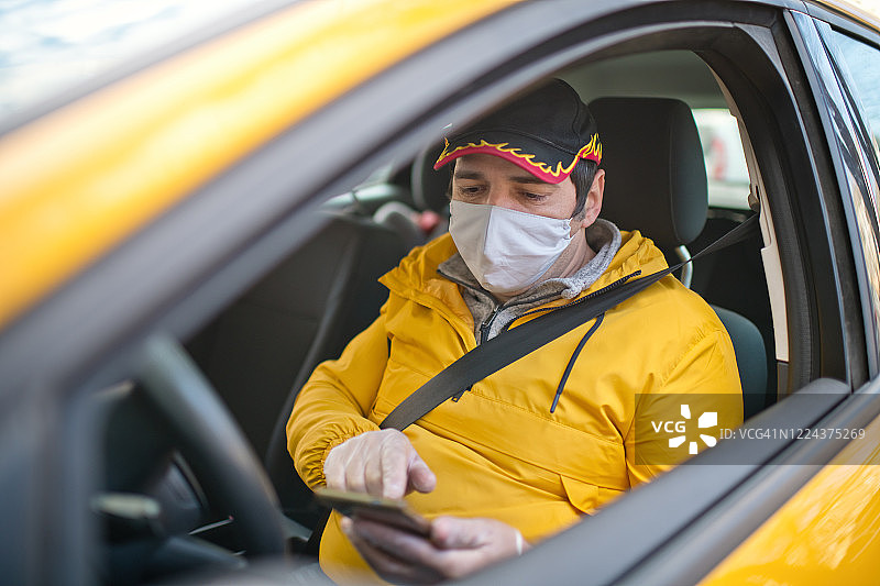 疫情期间，出租车司机戴着防护口罩在城市街道停车并使用智能手机图片素材