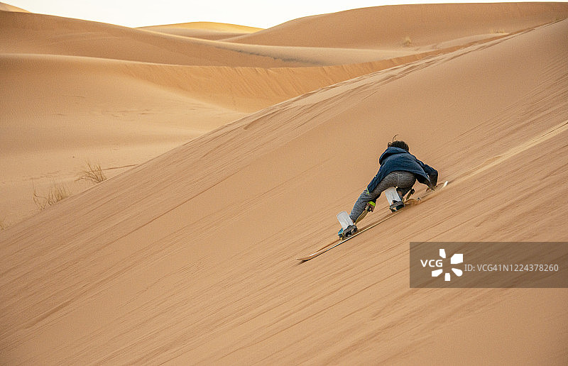 日落时分，小男孩在非洲摩洛哥撒哈拉沙漠玩滑沙图片素材