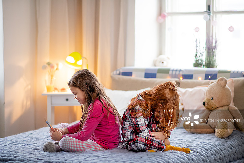 床上两个小女朋友，一个在打电话，一个感到悲伤和失望图片素材
