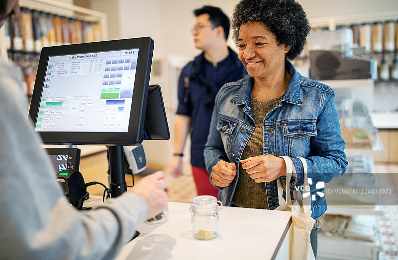 笑容满面的顾客站在零浪费商店的收银台旁，与店主在一起图片素材
