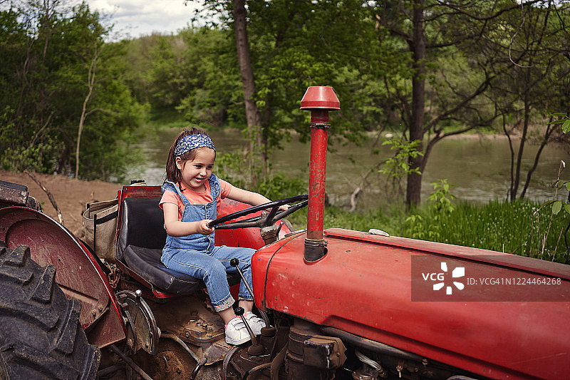 可爱的小女孩在家庭牧场玩耍，假装开拖拉机图片素材