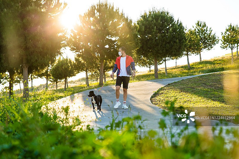 带着戴防护口罩的美国斯塔福梗犬行走的年轻男人图片素材