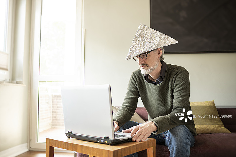 男人（51岁）戴着锡箔帽使用笔记本电脑图片素材