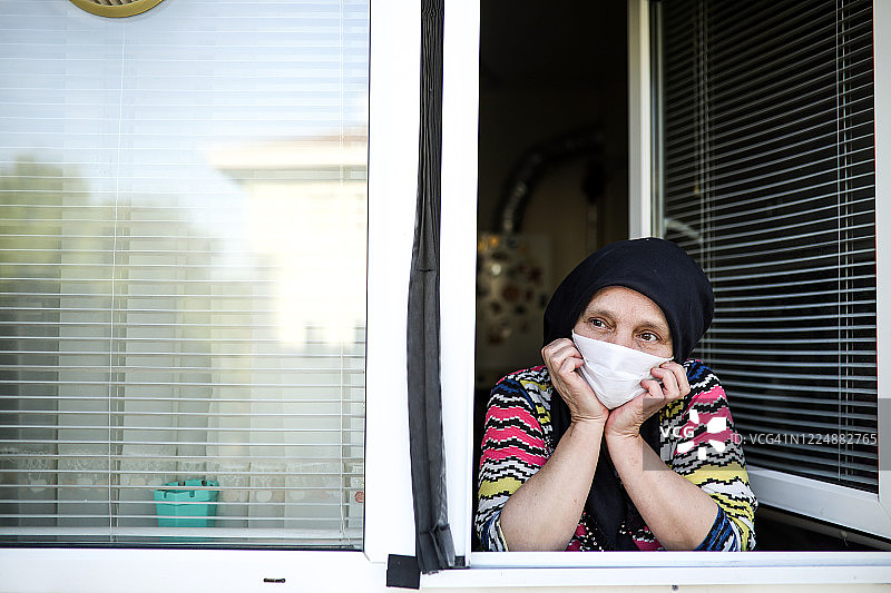 因隔离而无法出门的蒙面穆斯林妇女正在望向窗外图片素材