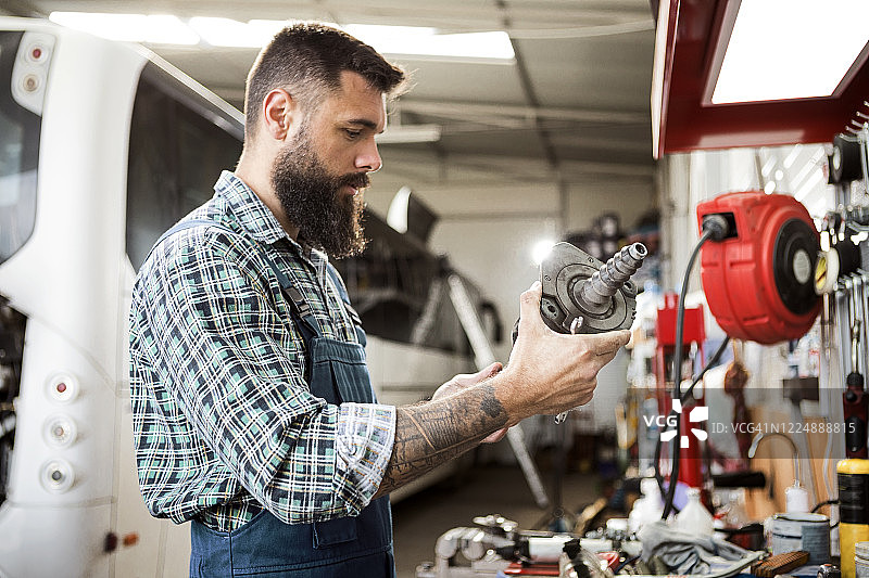 在汽车修理店修理公共汽车的修理工，拿着有问题的零件图片素材