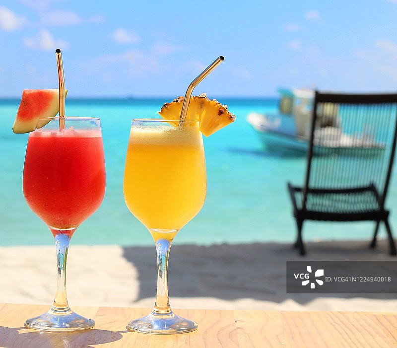 木桌上的西瓜汁和菠萝汁（蓝色海景背景）图片素材