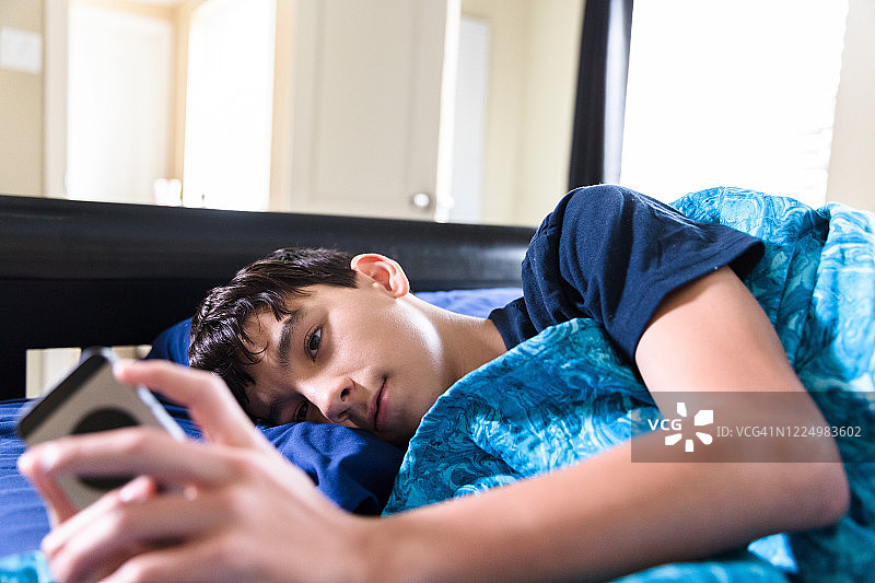 发烧的青少年男孩在床上给朋友发短信图片素材