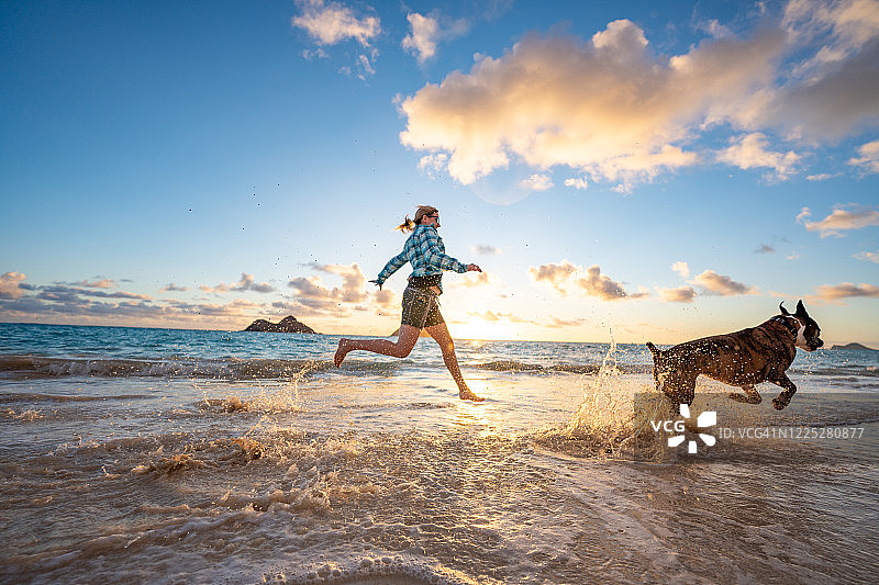 日出时分，女人和狗在沙滩上奔跑图片素材