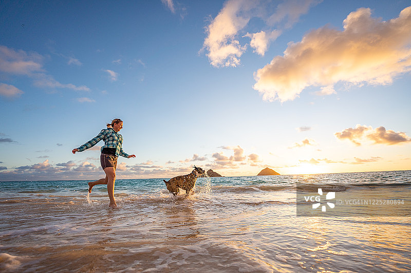 日出时分，女人和狗在沙滩上奔跑图片素材