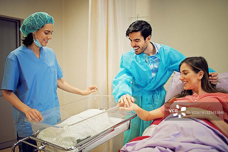 夫妇和他们的医生站在医院产房里，抱着一个新生婴儿图片素材
