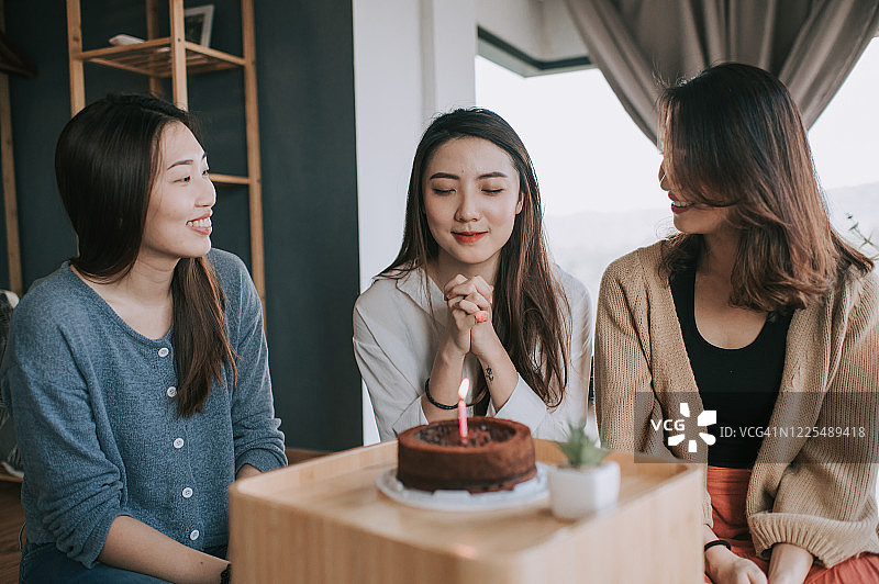 一位中国年轻漂亮女子在公寓里和朋友们一起庆祝生日，一起对着生日蛋糕许愿图片素材