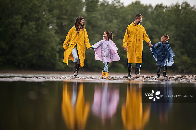 幸福的一家人穿着雨衣在雨中湖边散步图片素材