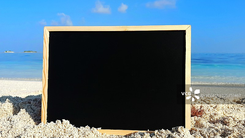 白色沙滩上的黑色黑板，可用于书写，海洋和天空模糊背景概念设计图片素材