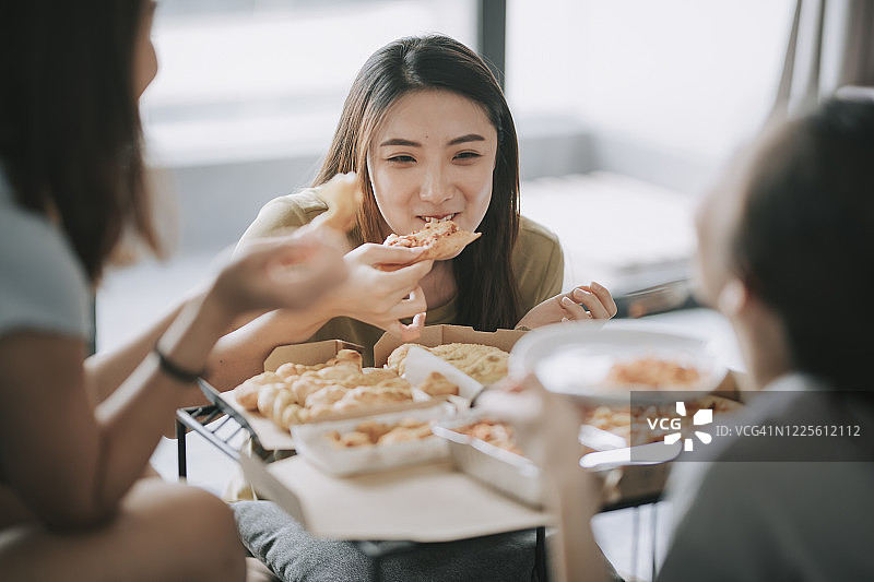 3个中国亚洲女性朋友在客厅里吃披萨图片素材