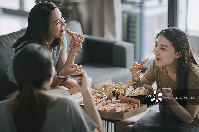 3个中国亚洲女性朋友在客厅里吃披萨图片素材