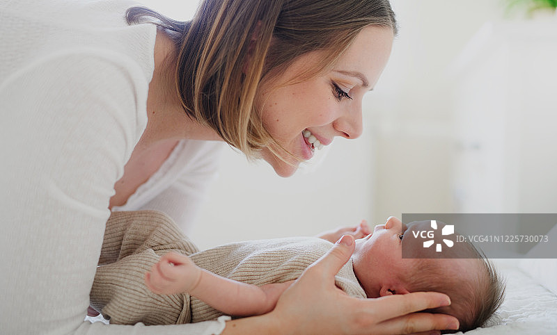 侧视图：女子在卧室里与新生婴儿交谈。图片素材