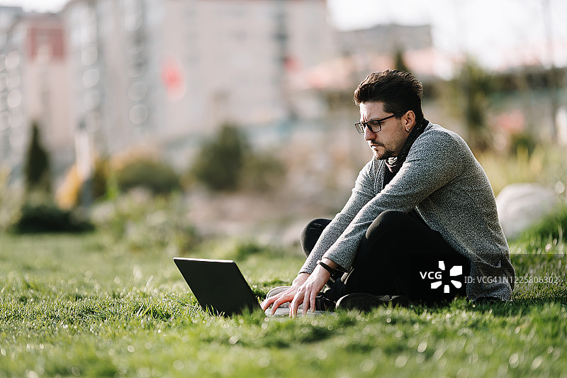 在城市公园草地上使用笔记本电脑的年轻人图片素材