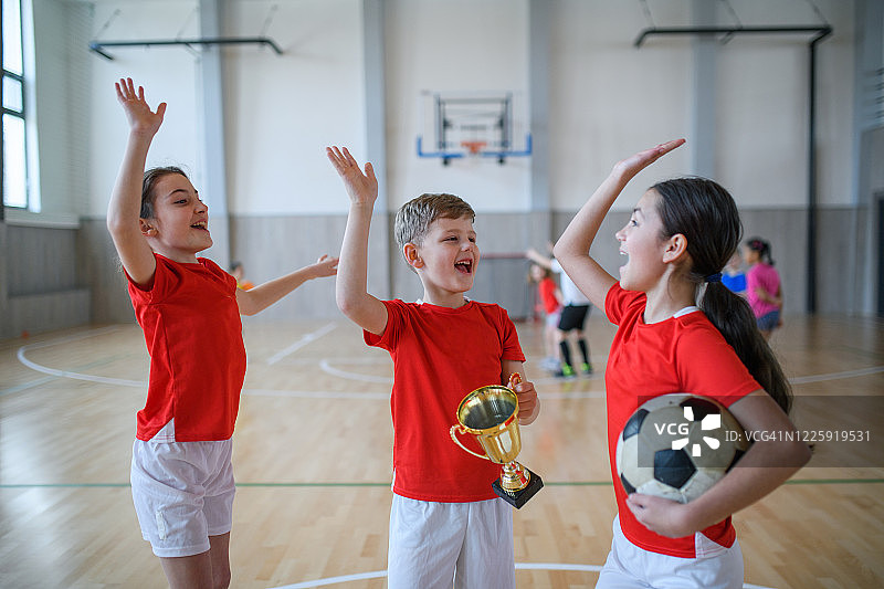 一群小孩在体育馆的课堂上用球和杯子欢呼的正面图图片素材