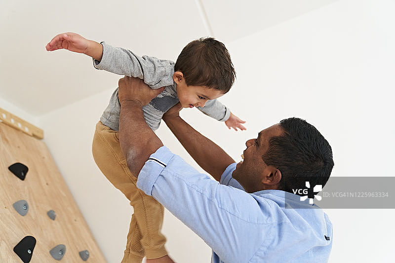 父亲高举儿子，父子俩都面带微笑，儿子张开双臂图片素材