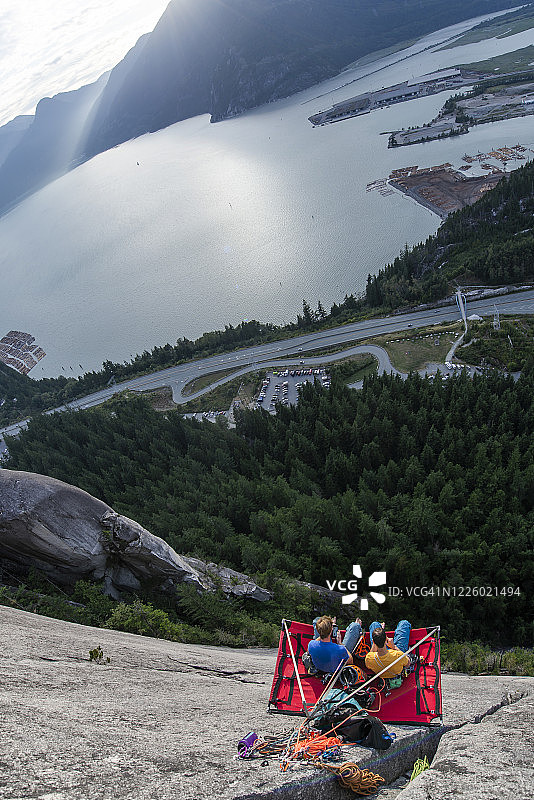 日落时分，两名男子坐在悬崖营地上，天空与大海交相辉映图片素材