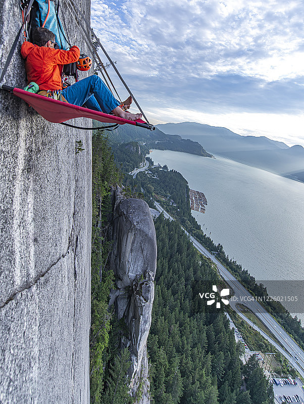 日落时坐在悬崖边整理装备的男子侧视图图片素材