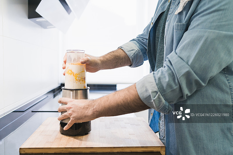 男人在厨房穿着牛仔衬衫烹饪。一位匿名人士将要打面粉、鸡蛋和牛奶的混合物图片素材