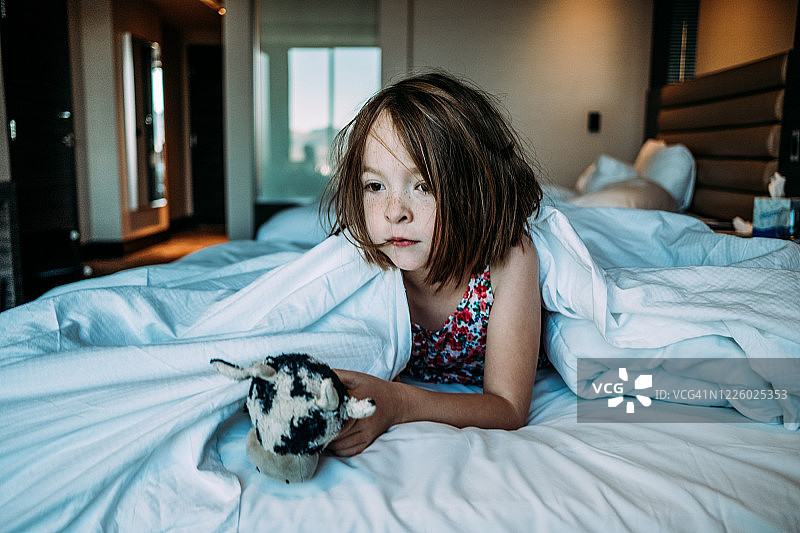在酒店床上醒来的年轻女孩，怀里抱着她的玩具图片素材