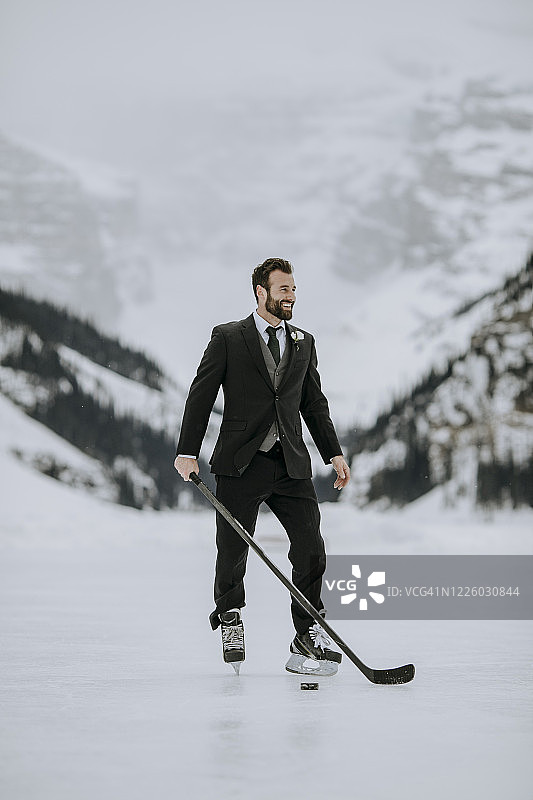 穿黑色西装、冰球鞋、拿着冰球杆的男人在冰冻的湖面上摆姿势图片素材