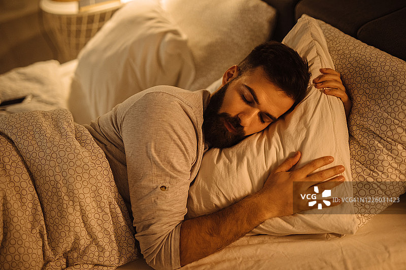 年轻男人抱着柔软的白色枕头在床上睡觉图片素材