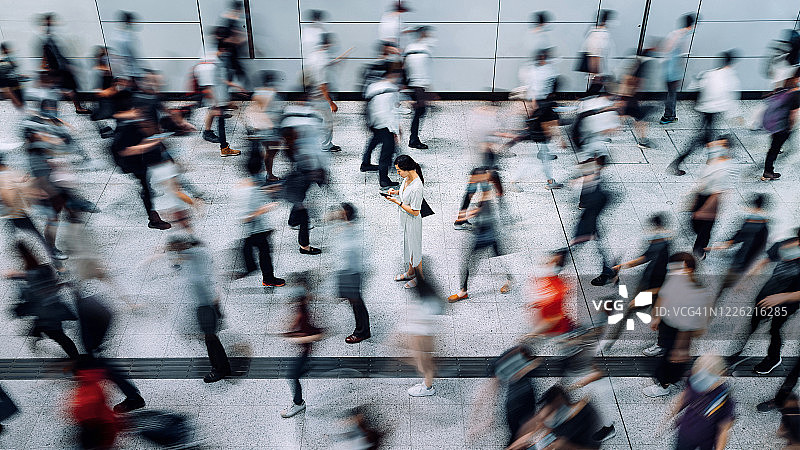 高峰时段在地铁站被通勤者包围的使用智能手机的年轻亚洲女性图片素材