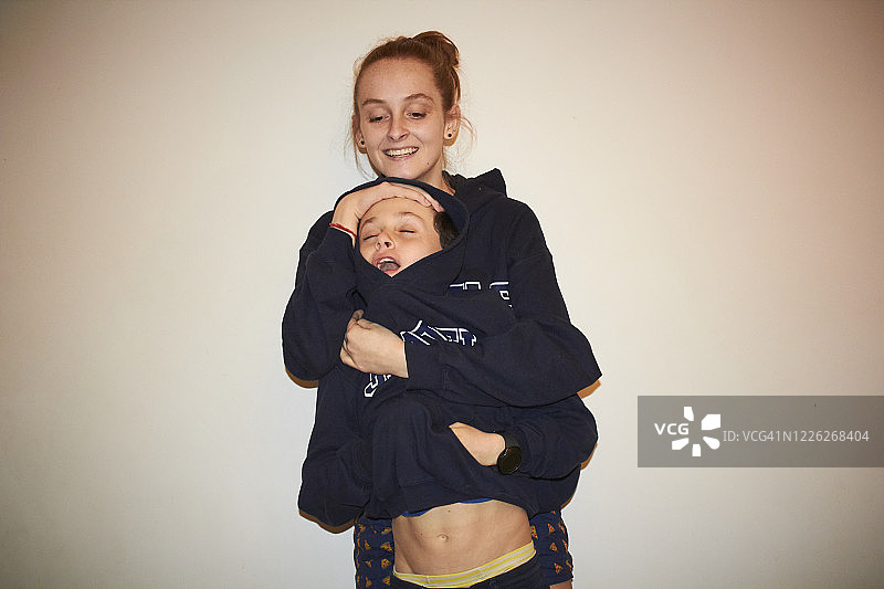 棕色卷发男孩和红发姐姐在白墙前穿着同款卫衣合影图片素材