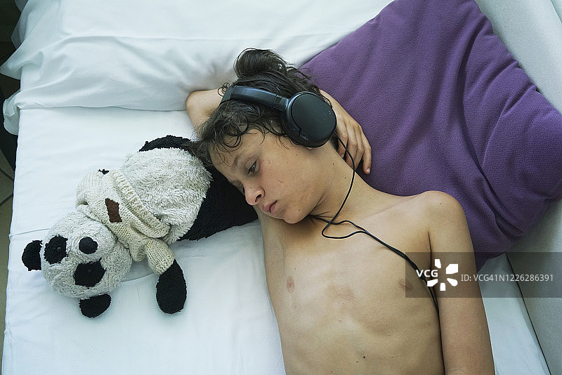 戴耳机躺在熊猫玩具旁的小男孩图片素材
